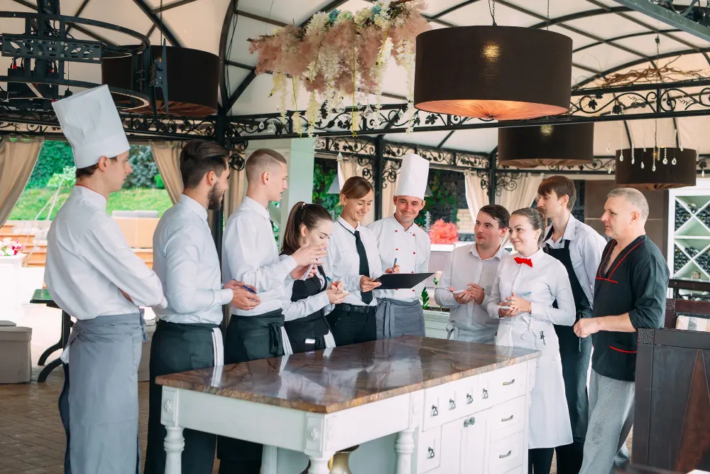 Chefs and staff gathered around kitchen table.